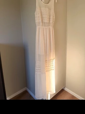 Lång vit spetsklänning H&M - Lång vit klänning med spetsdetaljer och transparenta partier. Klänningen är ärmlös och har en luftig, flowy passform med markerad midja. Perfekt för sommarens alla tillfällen och ger en romantisk vibe.
