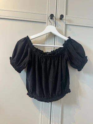 Svart offshoulder blus med broderi - Söt svart offshoulder blus med puffiga korta ärmar och elastiska band vid halsringning och midja. Storlek XS från Gina Tricot 🫶🏻