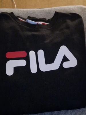 Fila sweatshirt  - Svart tröja från FILA med stor vit och röd logga på bröstet. Tröjan har rund halsringning och långa ärmar. 