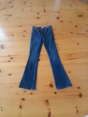 Blå bootcut jeans med utsvängda ben - Ett par blå bootcut jeans med klassisk femficksmodell och normal midja. Jeansen har utsvängda ben och är sydda i denim för en tidlös look. Perfekt för dig som gillar retrostil och vill ha ett par jeans som sticker ut.