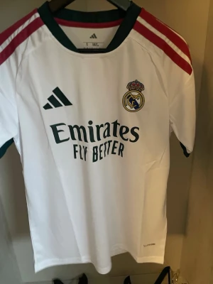 Real Madrid Fotbollströja 26/27 - Helt ny och trendig Real madrid 2026 / 2027 säsongs Hemma version fotbollströja. Nypris runt 1099kr. Passformen på tröjan är som en oversized t-shirt i storlek S. Tröjan kommer med original förpackning och skickas i förstärkt påse för att hindra skador eller slit under frakt. Kontakta vid funderingar, och kolla min profil om du vill se andra tröjor. 