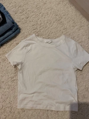 Vit basic t-shirt från Gina tricot  - En enkel och stilren vit t-shirt från gina. T-shirten har korta ärmar, rund halsringning och är gjord i mjuk bomull. Perfekt till jeans eller shorts för en clean look.