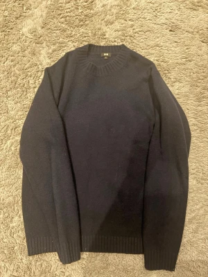 Mörkblå stickad Kashmir tröja från Uniqlo - Klassisk mörkblå stickad kashmir tröja från Uniqlo i storlek M. Tröjan har rund halsringning, långa ärmar och ribbade muddar vid ärmslut och nederkant. Perfekt för lager på lager och enkel att matcha med olika outfits.