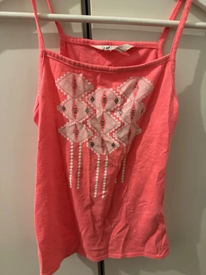 Korall / Rosa linnetopp - Snygg korall / rosa linnetopp från H&M med tunna axelband och ett grafiskt vitt tryck framtill.😊 Den är i storlek 146/152 men skulle även passa som xxs 
