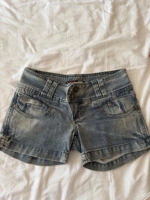 Blå jeans shorts med knappar - Snygga blå jeans shorts med dubbla knappar framtill och klassiska fickor. Shortsen har en lätt tvättad look.    Storlek 40 men skulle säga 36