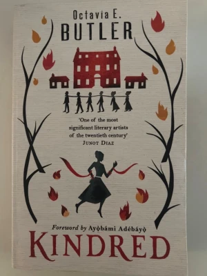 Kindred av Octavia E. Butler - Kindred är en roman av Octavia E. Butler med ett omslag i beige och svart, dekorerat med silhuetter, eldflammor och ett rött hus. Boken handlar om tidsresor, slaveri och identitet. Omslaget har illustrationer av Yeti Lambregts och förord av Ayọ̀bámi Adébáyọ̀.