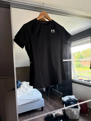 Svart tränings-tshirt Under Armour - Säljer en svart tränings-tshirt från Under Armour med korta ärmar och rund hals. Tillverkad i ett snabbtorkande funktionsmaterial som passar perfekt till gymmet eller löpning. Logga i vitt på bröstet för en sportig look. Prislappen sitter fortfarande på, endast testat tröjan. Jag beställde nämligen en i XS och denna i S då jag var osäker på storlek!😊