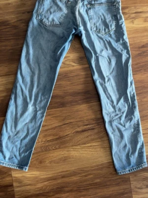 Ljusblå raka jeans - Säljer ett par ljusblå jeans med rak passform och klassisk femficksdesign. Jeansen har normal midja och är tillverkade i denim. Perfekta för en avslappnad och trendig look.
