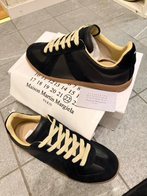 Svart Maison Margielas  - Tjena jag säljer ett par vackra maison Margielas i storlek 42 svart då det inte kommer till användning och den är helt oanvänd skick. Dustbag, kortet, skolådan och skorna medföljs i köpet! Vid snabb affär tillkommer ett bättre pris!