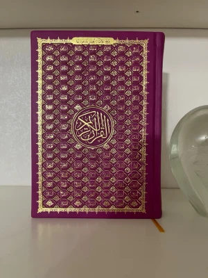 Vacker lila koran med engelsk översättning  - Koran med arabisk text och engelsk översättning. Vacker lila hårdpärm med gulddetaljer och guldfärgade sidor. I mycket fint skick. Perfekt för egen läsning eller som present. Köptes för cirka 900kr