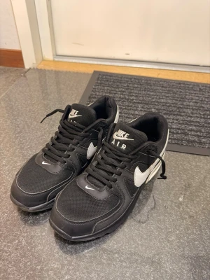 Svarta Nike Air sneakers med vit swoosh - Snygga svarta Nike Air sneakers med vit swoosh på sidan och vita detaljer. Skorna har en klassisk låg siluett, snörning och ovandel i mesh och syntetmaterial för bra komfort och stil. Perfekta för dig som gillar streetwear och sportig look.