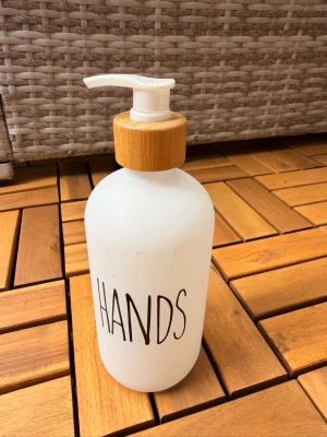 Ny Vit tvålpump med bambulock - Stilren tvålpump i matt vit plast med texten 'HANDS' i svart på framsidan. Pumpen har ett lock i bambu som ger en naturlig känsla och passar perfekt i badrummet eller köket. Enkel att fylla på och använda för flytande tvål.