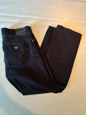 Svarta jeans från Armani Jeans - Snygga svarta jeans från Armani Jeans med klassisk femficksmodell och silverfärgad logga på bakfickan. Jeansen har normal midjaben.Materialet känns mjukt och slitstarkt, perfekt för en trendig vardagslook. Litet slitage inuti höger ficka som verkligen inte syns eller påverkar skriv vid fundering!