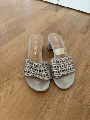 Silvriga sandaler med blockklack - Säljer ett par silvriga sandaler från Zosdon med öppen tå och bred rem i glittrande nätmönster. Skorna har en bekväm blockklack och mjuk innersula. Perfekta för dig som vill ha något extra till outfiten.