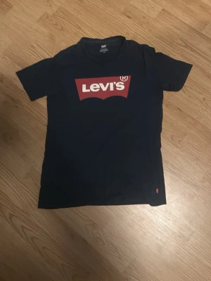 Svart Levi's t-shirt med logga - Snygg svart t-shirt från Levi's med den klassiska röda loggan framtill. T-shirten har korta ärmar och rund halsringning. Tillverkad i mjuk bomull som är skön att bära. Perfekt till jeans eller shorts för en avslappnad look.