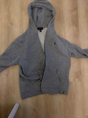 Polo Ralph Lauren zip hoodie grå - Säljer en grå Polo Ralph Lauren zip hoodie. Använd men i bra skick. Fodrad/tjockare modell med dragkedja och broderad logga på bröstet. Säljes då den inte används längre. Kontakta gärna mig vid frågor