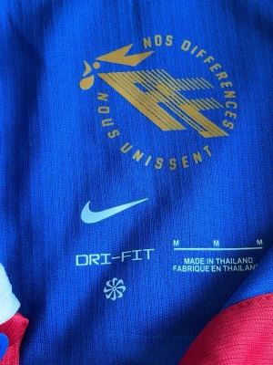 Frankrikes vm tröja - Snygg blå fotbollströja från Nike med Dri-FIT-material som håller dig torr. Tröjan har korta ärmar, grafiskt mönster i olika blå nyanser och tryck i gult framtill med texten 'Nos différences nous unissent'. Perfekt för träning eller match.