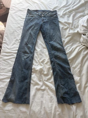Blå bootcut jeans med rå kant - Säljer ett par blå bootcut jeans med råa, avklippta benslut. Jeansen har klassisk femficksdesign och låg midja. Tillverkade i denim med en lätt tvättad look. Perfekta för dig som gillar en avslappnad och trendig stil. Storlek 29/34 men avklippta där nere, går ner till marken på mig som är 175