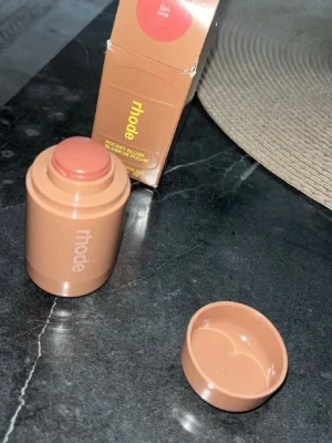 Rhode Pocket Blush Tan Line - Krämrouge i stickformat från Rhode i nyansen Tan Line. Färgen är en varm, naturlig brunrosa ton som ger kinderna en fräsch glow. Förpackningen är kompakt och cylinderformad i beige plast, perfekt att ha med i väskan.