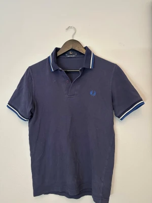 Marinblå piké från Fred Perry  - Pris kan diskuteras! Mörkblå Fred Perry pike i bra skick. På grund av solblekning kan den uppfattas som lite lila nyans i vissa ljus. Sitter som en Xs/S 