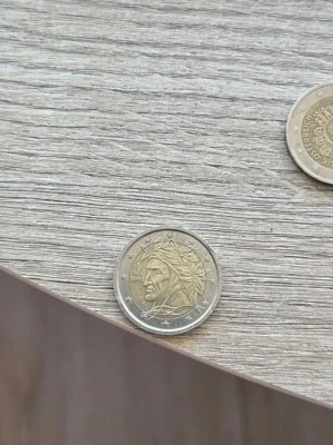 Två euromynt med motiv - Säljer två euromynt, ett med ett porträtt av Dante Alighieri och stjärnor runt kanten. Mynten är i metall med silverfärgad kant och guldfärgad mitt. Perfekt för dig som samlar på utländska mynt eller gillar unika detaljer.