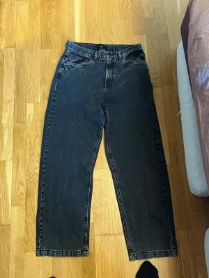 Grå raka jeans från ADPT - Säljer ett par grå denimjeans från ADPT med rak passform och klassisk femficksdesign. Jeansen har normal midja och stängs med dragkedja och knapp. Perfekta för en avslappnad och trendig look. 32/34