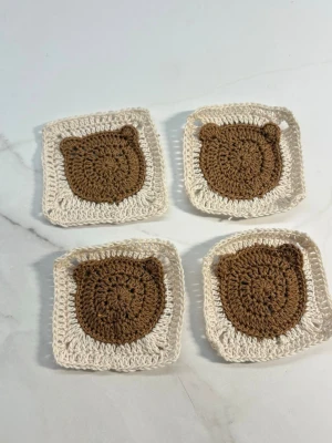 Virkade underlägg med björnmotiv - Fyra handgjorda virkade underlägg i beige och brunt med sött björnmotiv. Perfekta att ha under koppar eller glas för att skydda bordet och ge en gullig touch till dukningen. Underläggen är fyrkantiga och mjuka, tillverkade i bomullsgarn.