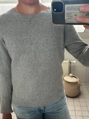 Ljusgrå stickad tröja - En stilren ljusgrå stickad tröja med rund halsringning och långa ärmar. Tröjan har en enkel design med ribbstickade muddar vid ärmslut och nederkant. Perfekt att matcha med jeans för en avslappnad look. Har använt den många gånger och den har blivit lite tussig.