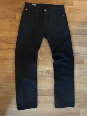 Svarta raka jeans - Säljer ett par svarta jeans med rak passform och klassisk femficksdesign. Jeansen har knappgylf och detaljer i metall. Materialet är denim i bomull och färgen är djupsvart. Perfekta för dig som gillar en clean och tidlös look. Storlek W32/L32