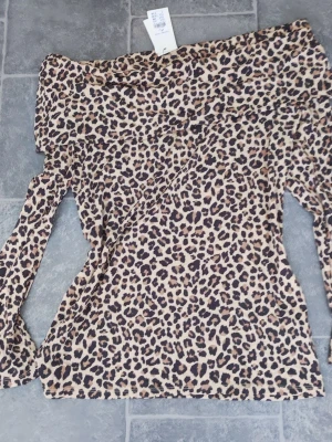 Leopardmönstrad offshoulder topp XL - Säljer en snygg offshoulder topp i leopardmönster. Toppen har långa ärmar och är tillverkad i ett mjukt, stretchigt material som sitter bekvämt. Perfekt för dig som vill sticka ut med ett djurmönster och gillar trendiga plagg.