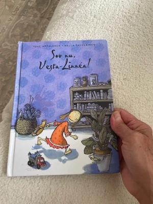 Sov nu, Vesta-Linnéa! - En illustrerad barnbok med hårda pärmar och färgglada teckningar. Boken handlar om Vesta-Linnéa och är skriven av Tove Appelgren och illustrerad av Salla Savolainen. Omslaget är lila med en tecknad flicka och inredningsdetaljer.nypris 209kr