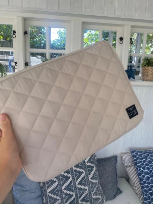 Beige quiltad datorväska - Snygg quiltad datorväska i beige från 157 Denim Makers. Väskan har ett stilrent rutmönster och en mjuk vadderad känsla som skyddar din laptop. Perfekt för dig som vill ha en enkel men trendig look till din dator.