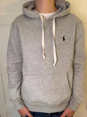 Grå Ralph lauren hoodie - Snygg grå Ralph lauren hoodie i 9/10 skick. Modellen är 176 och väger 63kg. Kan gå ner i pris vid snabb affär.