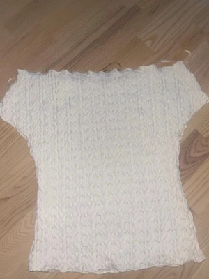 Vit ribbad topp med korta ärmar - Säljer en vit topp med ribbad struktur och korta ärmar. Toppen har en lätt croppad passform och är tillverkad i ett stretchigt material som formar sig snyggt efter kroppen. Perfekt för dig som gillar en enkel och clean stil.