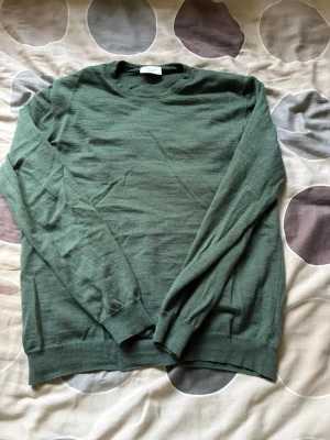 Grön stickad tröja från Profuomo - Snygg grön stickad tröja från Profuomo i storlek M. Tröjan har rund halsringning, långa ärmar och ribbade muddar vid ärmslut och nederkant. Perfekt för lager på lager och enkel att matcha med olika outfits.