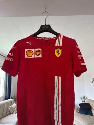 Röd Ferrari F1 formula 1 formel 1 t-shirt - vintage - Ovanlig och unik, 2020 Leclerc edition. Röd Ferrari t-shirt från Puma med tryckta loggor från Shell, UPS och Ferrari-märket på bröstet. T-shirten har vita, gröna och röda racingränder samt sponsorloggor på ärmarna. Perfekt för motorsportfans som vill sticka ut.