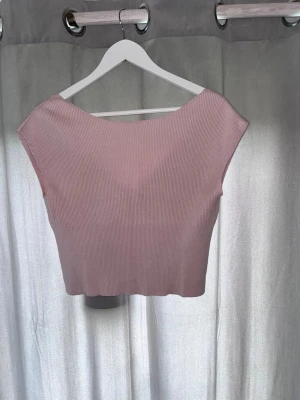 Ljusrosa ribbad croppad topp - Säljer en ljusrosa croppad topp med v-ringning framtill och breda axelband. Toppen är ribbad och har en mjuk, stretchig känsla som passar perfekt till jeans eller kjol. Enkel men snygg design som är lätt att matcha.