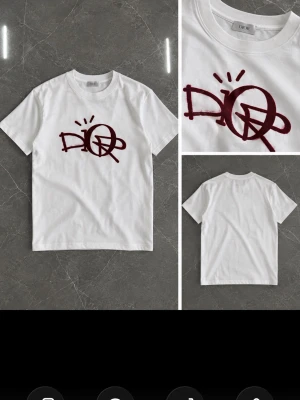Vit t-shirt med vinrött dior - Vit t-shirt med ett stort vinrött graffiti-inspirerat tryck på bröstet. Klassisk rund hals och korta ärmar. Perfekt för dig som gillar streetwear och vill sticka ut med en unik design.