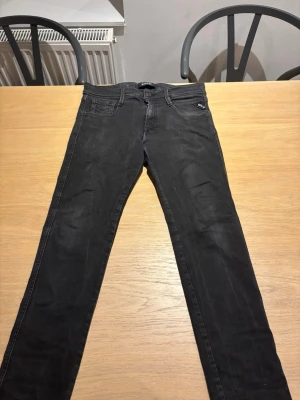 Svarta slim fit replay jeans - Snygga svarta slim fit jeans med fem fickor och dragkedja. Jeansen har klassisk design med raka ben och detaljerade sömmar på bakfickorna. Perfekta för en stilren och avslappnad look.