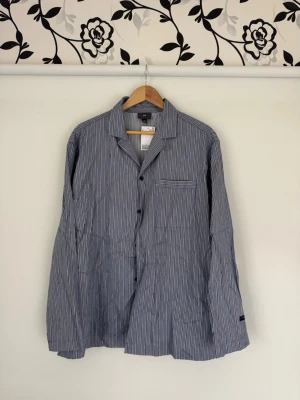 Randig pyjamaströja från H&M XL - Snygg blåvit randig pyjamaströja från H&M i storlek XL. Klassisk modell med knappar framtill, bröstficka och mjukt material. Perfekt för chilliga kvällar eller lata morgnar. Aldrig använd. Nypris med pyjamasbyxor 43€ eller ca 450:-