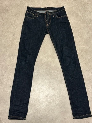 Nudie jeans  - Snygga mörkblå skinny jeans med klassiska fem fickor och kontrastsömmar. Jeansen har en smal passform och är tillverkade i ett stretchigt denimtyg som sitter tajt längs benen. Perfekta för en trendig och avslappnad stil.