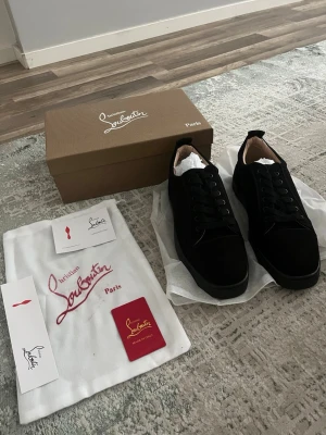 Svarta sneakers från Christian Louboutin - Stilrena svarta sneakers från Christian Louboutin i mocka med klassisk låg siluett och svarta skosnören. Insidan är fodrad i beige läder och skorna har diskreta detaljer som ger en lyxig känsla. Perfekta för dig som vill ha något exklusivt och tidlöst.