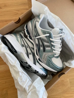 Asics Gel Kayano 14 - Snygga sneakers från Asics i vitt och ljusgrått med detaljer i silver. Skorna har mesh-ovandel för bra ventilation, klassisk snörning och en bekväm, stötdämpande sula. Perfekta för dig som gillar sportig stil och komfort.