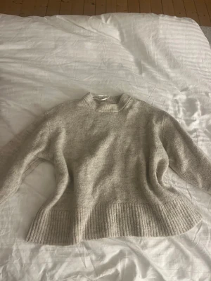 Beige stickad tröja från Gina Tricot - Mysig beige stickad tröja från Gina Tricot med rund halsringning och bred ribbstickad kant nedtill och vid ärmsluten. Tröjan har en avslappnad passform och är perfekt för kyliga dagar.