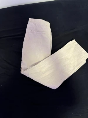 Beige linnebyxor med resårmidja - Snygga beige linnebyxor med avslappnad passform och resår i midjan. Byxorna har raka ben och en bakficka för en clean look. Perfekta för en chill och stilren outfit under varma dagar.
