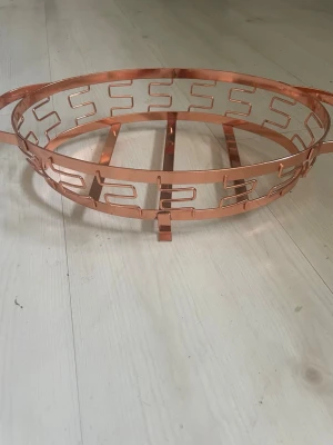 Kopparfärgad metallbricka med mönster - Säljer en rund bricka i kopparfärgad metall med dekorativt geometriskt mönster runt kanten. Brickan har två handtag och små fötter undertill, perfekt som dekoration eller för servering. Snygg detalj till hemmet.passat att sätta i en ugnsform i