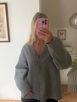 Grå oversized cardigan jacka - Grå cardigan jacka med v-ringad hals och långa, vida ärmar. Jackan har en minimalistisk look utan synliga knappar eller dragkedja och är oversized för en avslappnad stil. Passar perfekt till lager på lager under höst och vinter.
