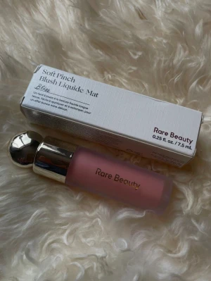 Rare Beauty Liquid Blush  - Rare Beauty Liquid Blush. Flytande rouge i en matt, ljusrosa ton med guld kork och frostat glas. Perfekt för en naturlig look och enkel att applicera med den smidiga applikatorn. .