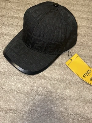 Svart keps från Fendi med FF-mönster - Snygg svart keps från Fendi med det klassiska FF-monogrammet invävt i tyget. Kepsen har böjd skärm och justerbar passform. Materialet är textil med en exklusiv känsla och detaljer i svart. Perfekt för dig som gillar streetwear och designeraccessoarer.