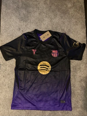 BarcaFotbollströja  - Säljer en svart och lila FCBarcelona matchtröja med LamineYamal och nummer 10 på ryggen. Tröjan har guldiga detaljer-logga på bröstet och  -tryck. Korta ärmar och sportig passform, perfekt för fotbollsträning eller match.